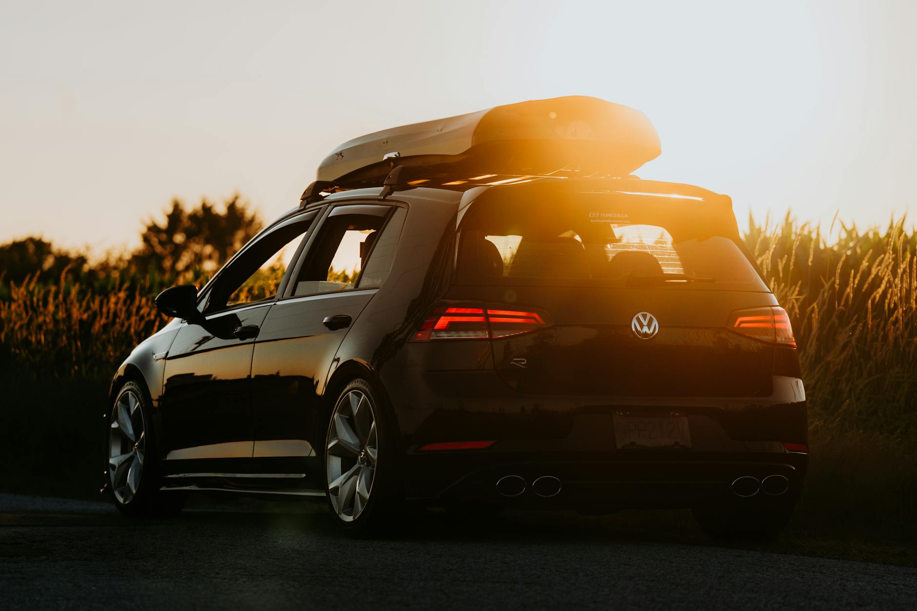 Czarny samochód z boxem dachowym zaparkowany na wiejskiej drodze o zachodzie