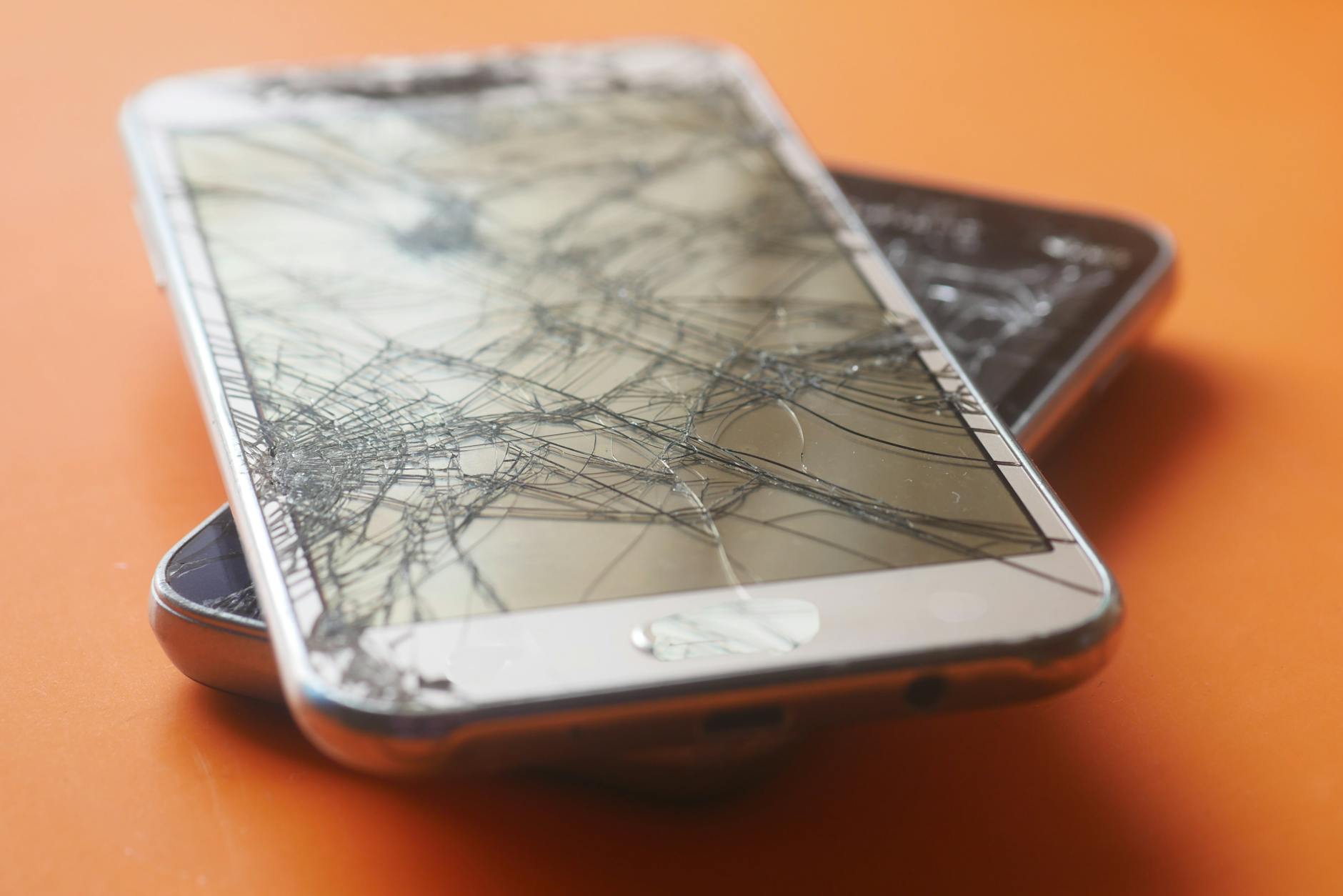 Dwa potłuczone ekrany smartfonów na pomarańczowym tle